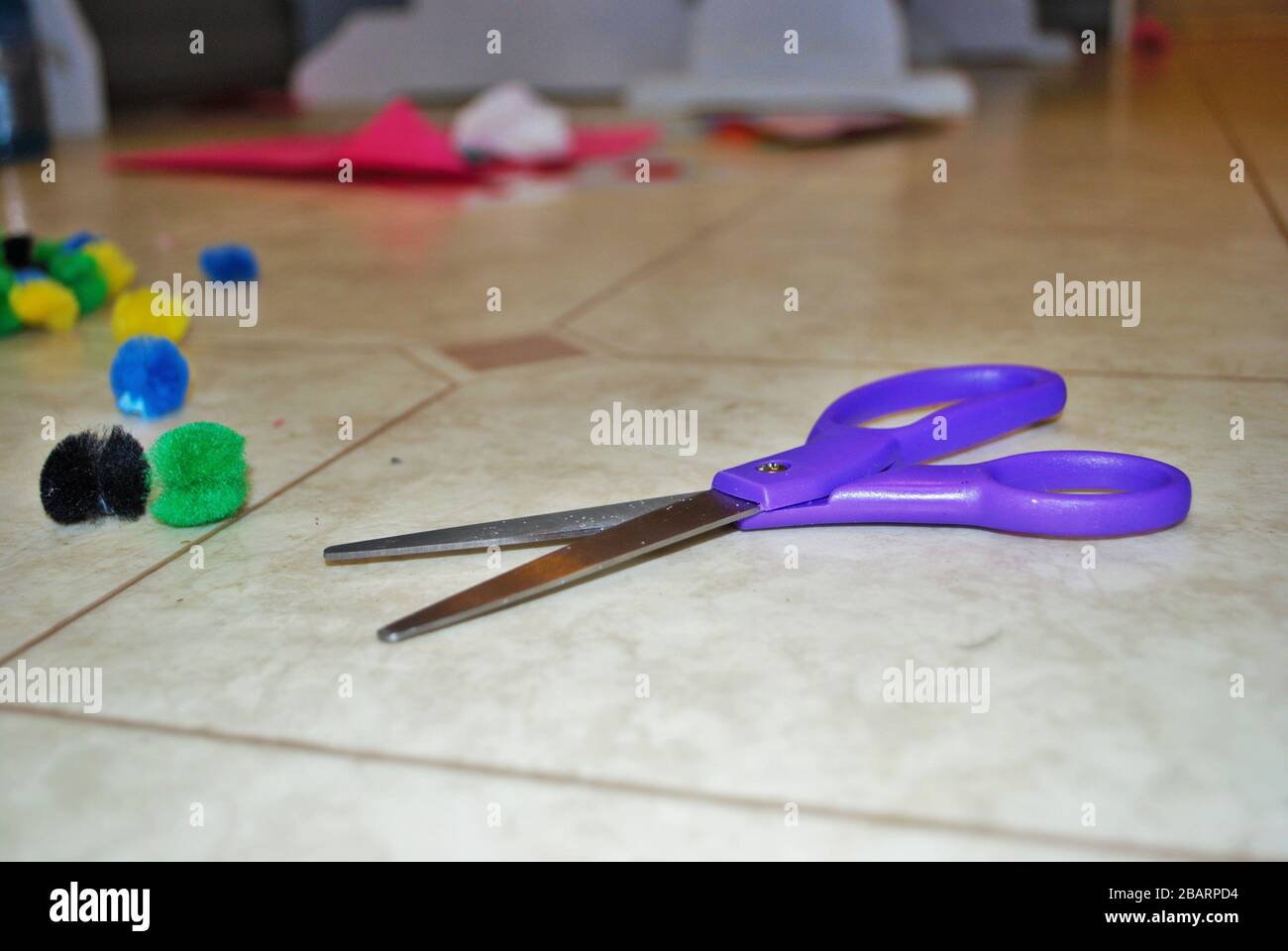 Multi colored cotton balls glue and scissors on a linoleum floor during