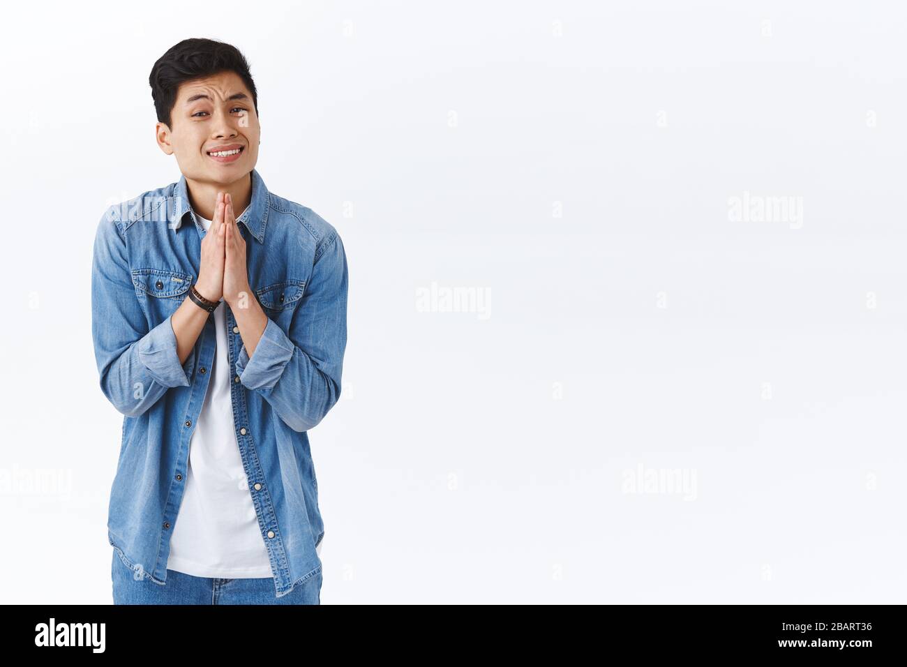 Portrait of clingy handsome asian guy need something asap, hold hands in pray, pleading or asking for help, begging person, grimacing standing white Stock Photo