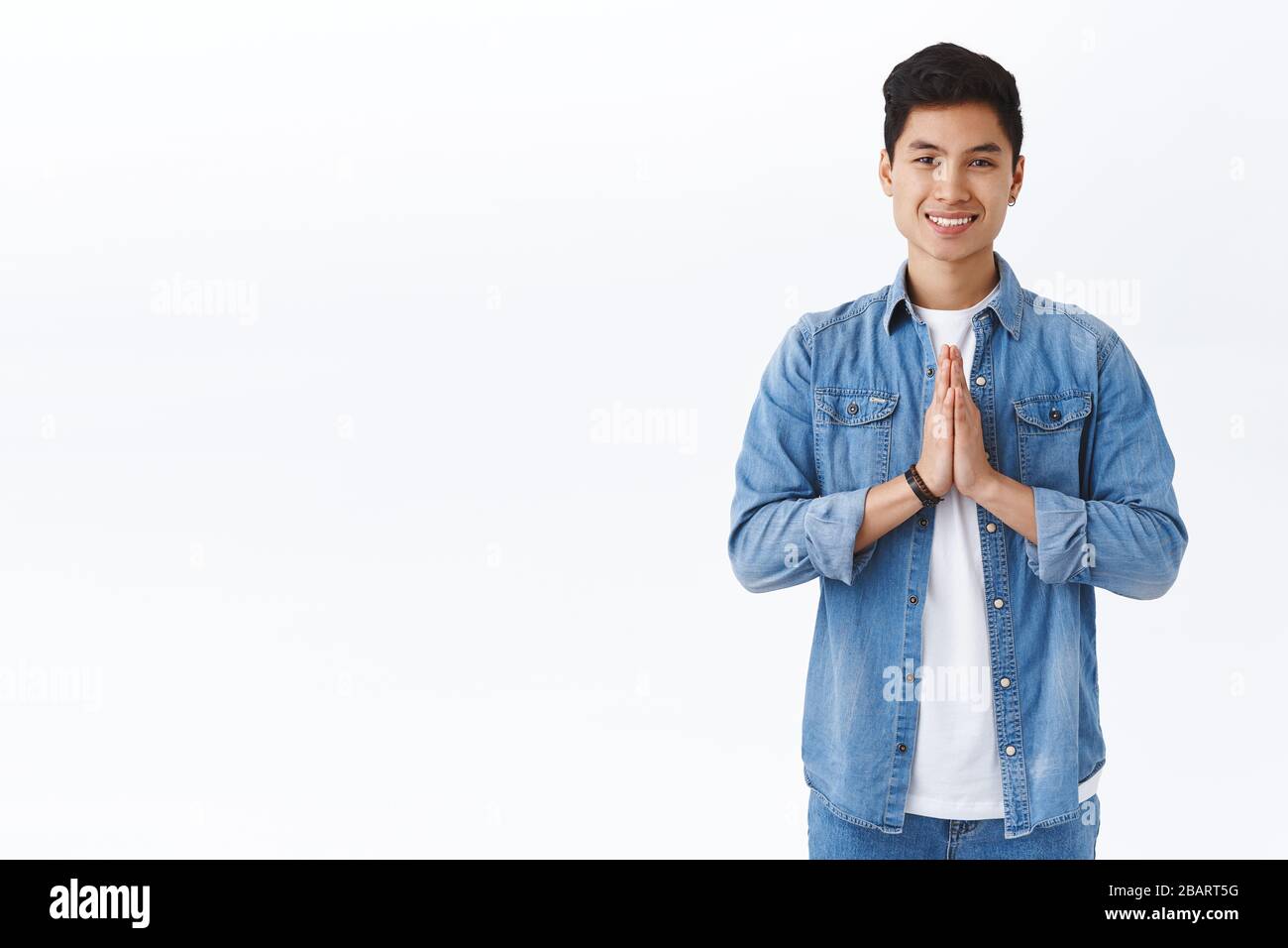 Portrait of handsome young male student smiling, thanking for help, hold hands in pray, have faith or hope, standing white background, appreciate help Stock Photo