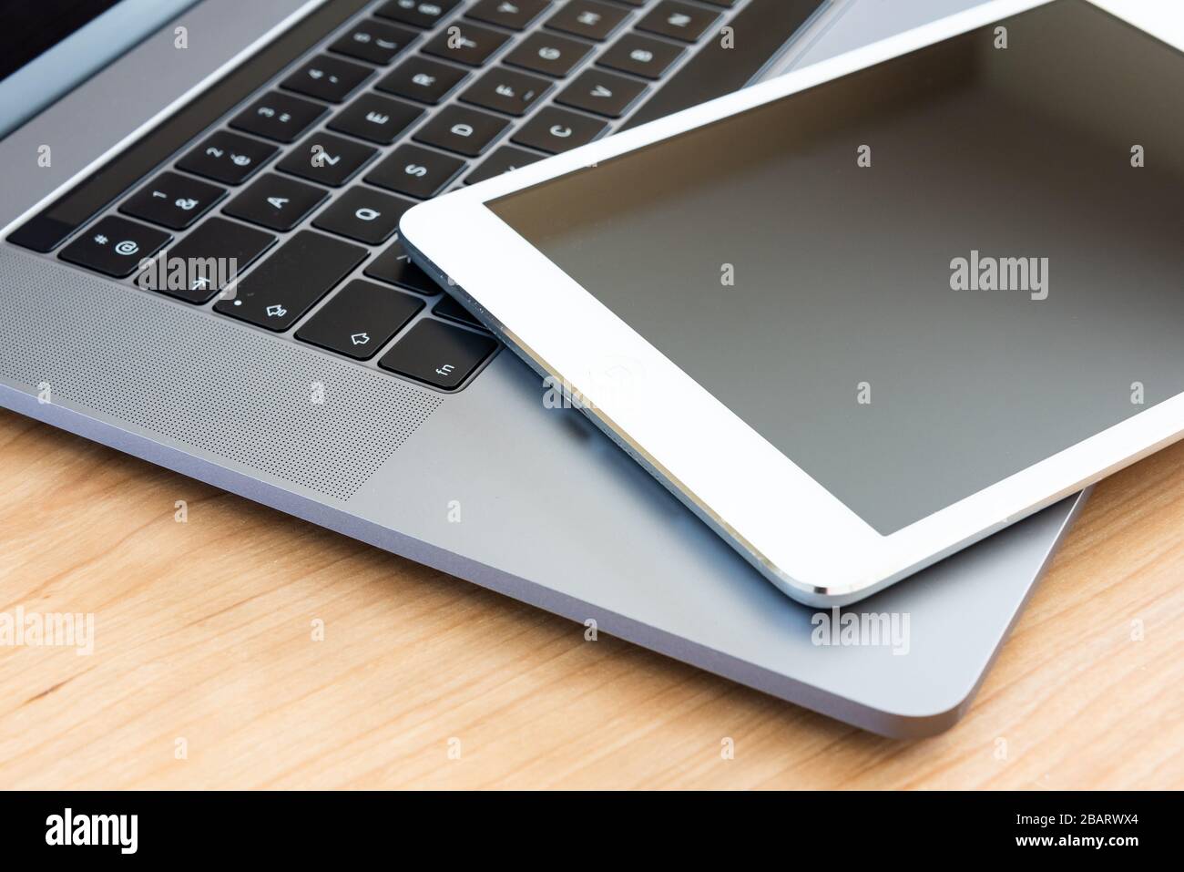 A white tablet and a laptop computer on a wooden surface. Stock Photo