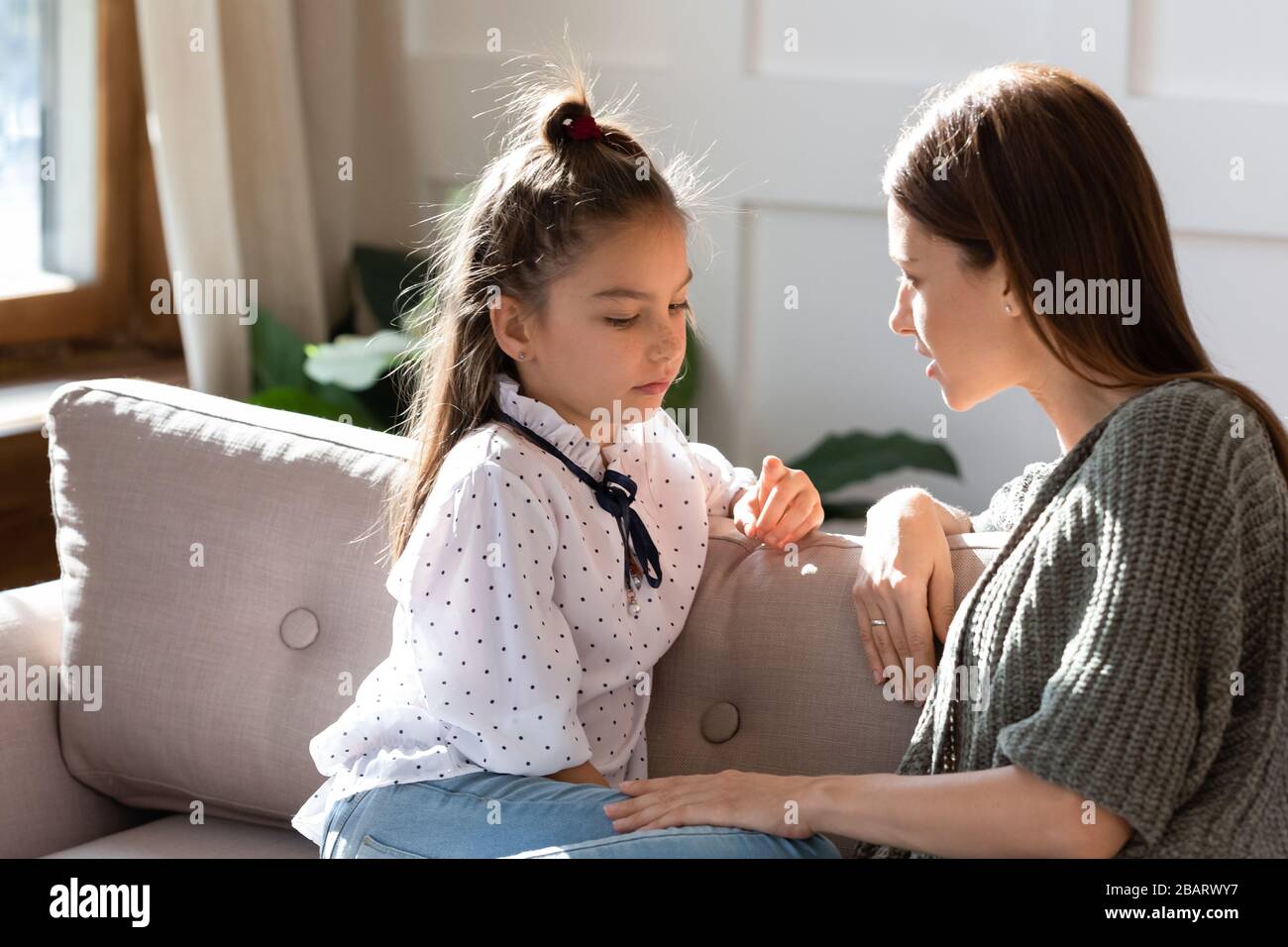 Upset small schoolgirl having trustful conversation with mother. Stock Photo