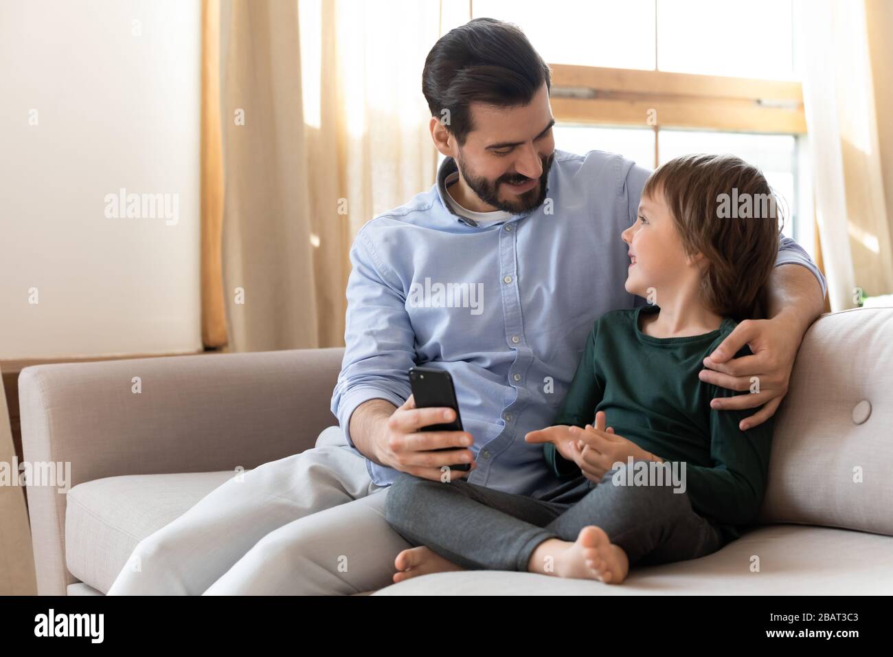 Happy dad cuddling small child son, showing funny mobile app. Stock Photo