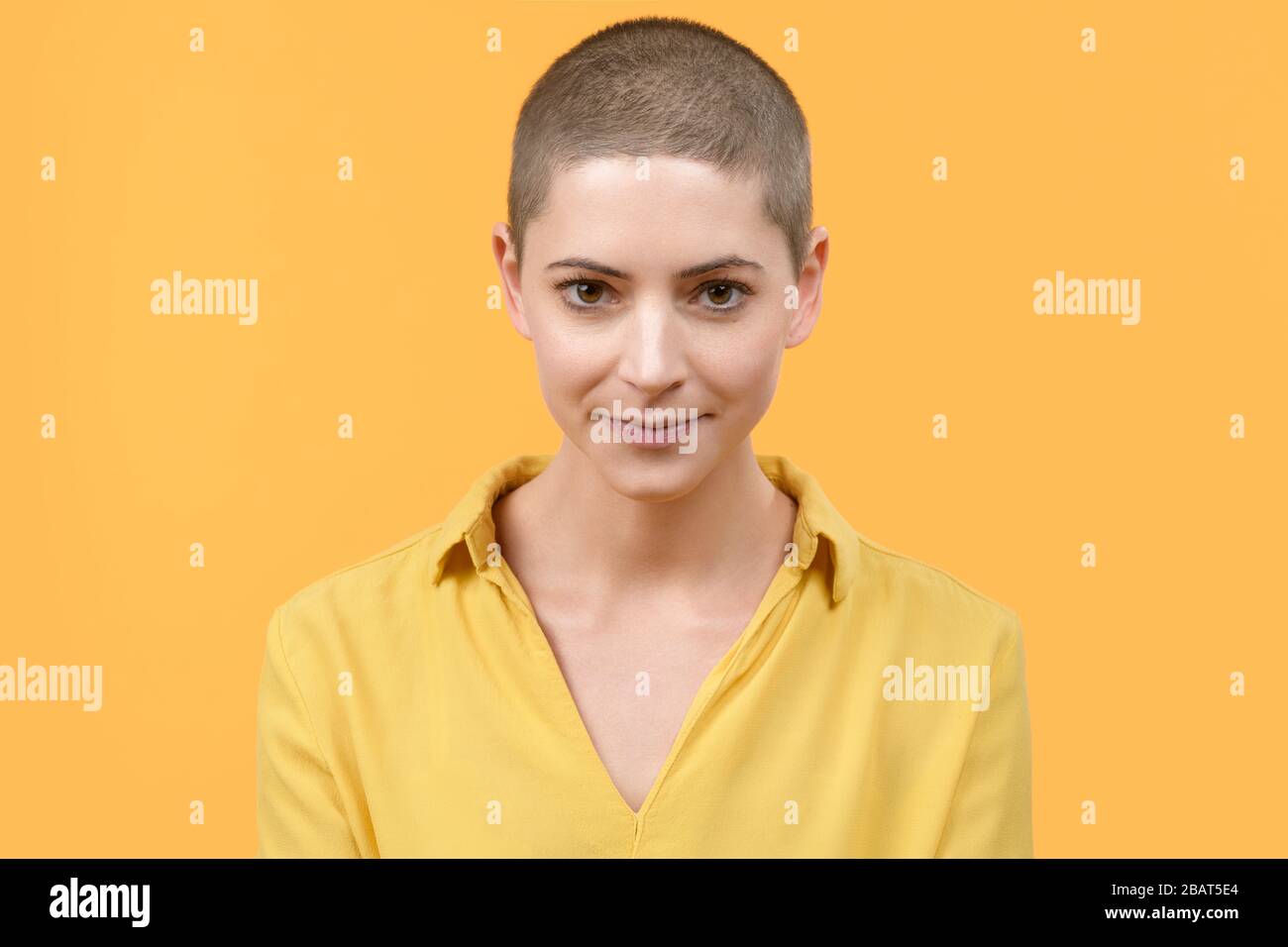 Studio portrait of a beautiful young caucasian woman with shaved head against bright yellow background. Cancer survivor portrait. Stock Photo