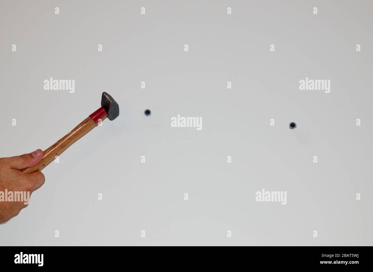 Hammering plastic screw anchor plugs into a concrete wall Stock Photo