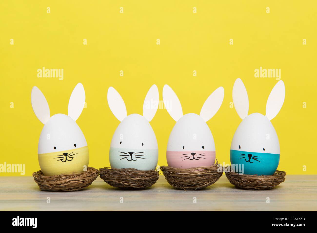 Easter eggs with bunny faces in nest on a yellow background with space for copy Stock Photo