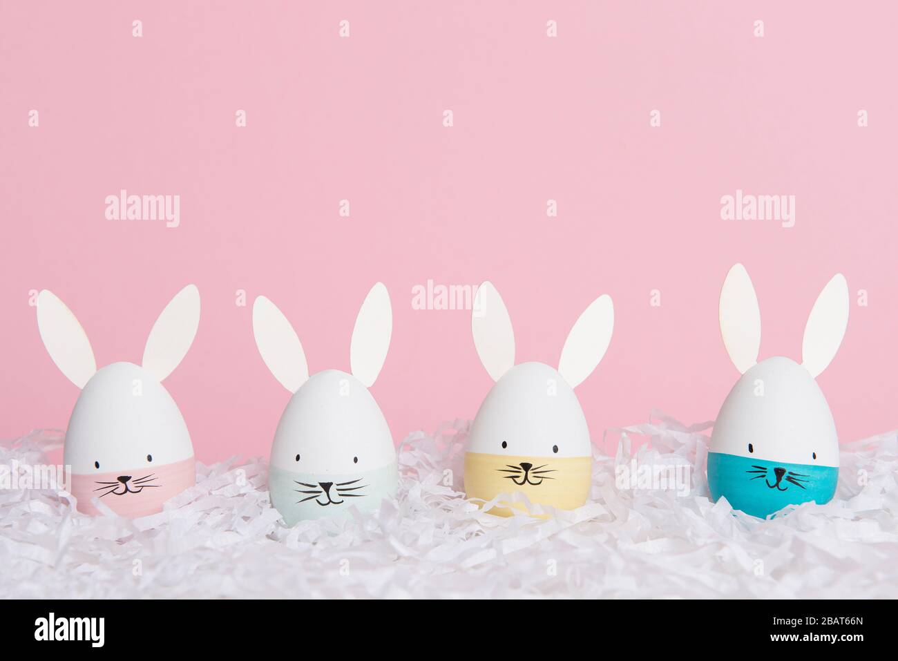 Easter eggs with bunny faces in nest on a pink background with space ...