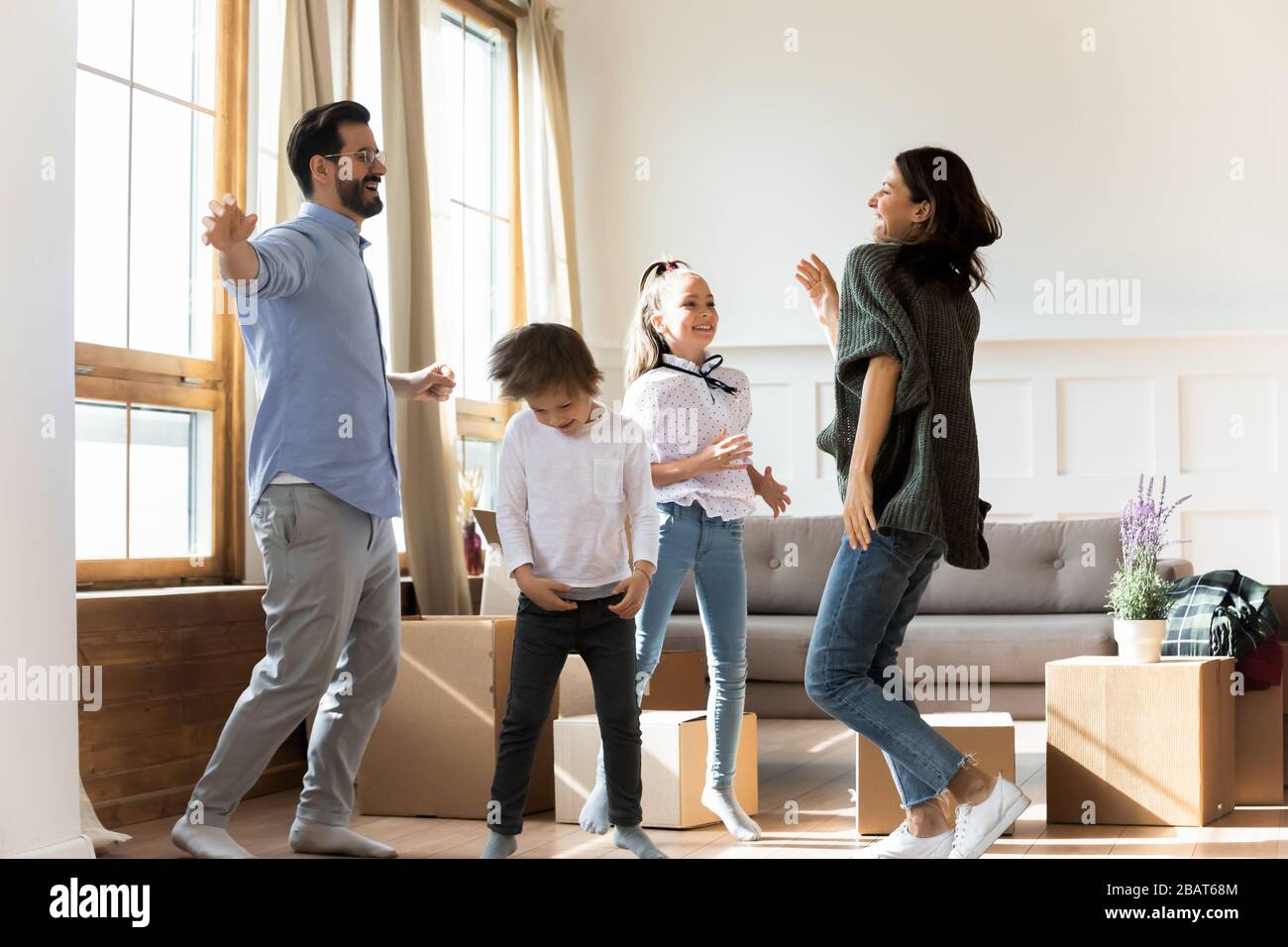 Overjoyed young parents dancing to energetic music with small kids ...