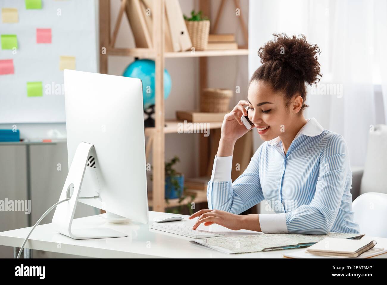 Tour agent sitting at table in office answering phone call using computer joyful Stock Photo