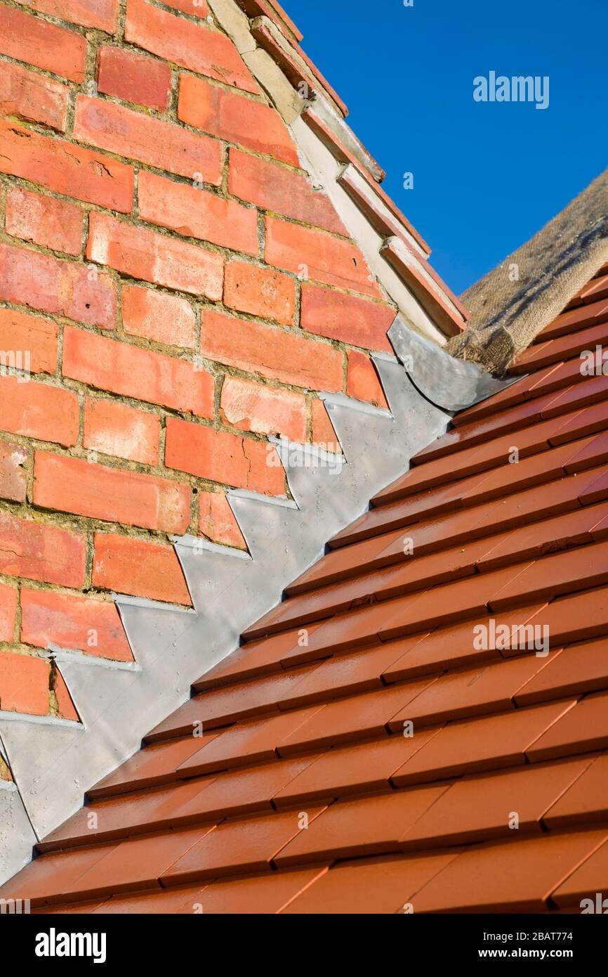 New plain red clay tiles and lead flashing detail on a pitched roof in the UK Stock Photo