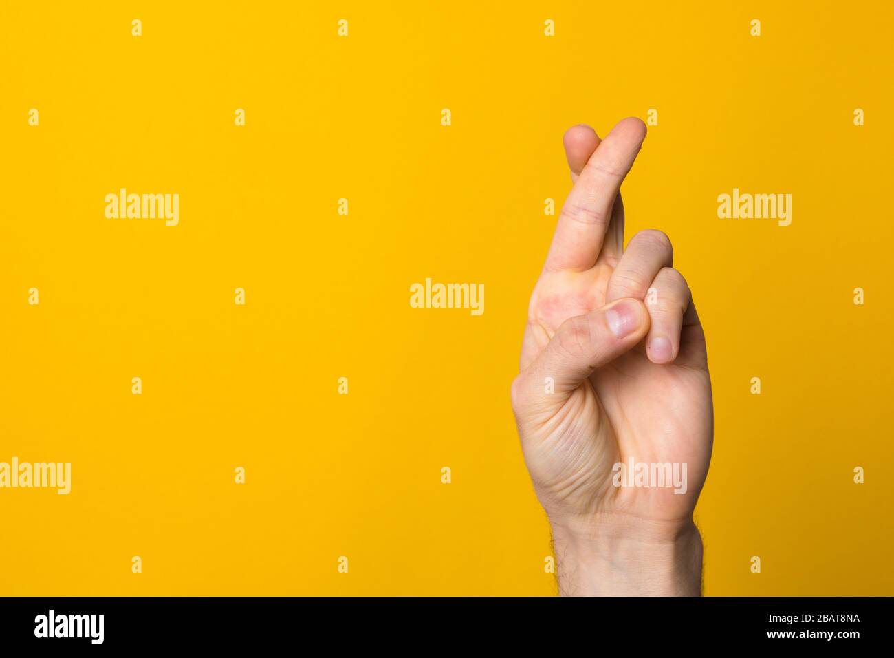 fingers crossed hope sign. close up man hand symbolising faith against yellow background Stock Photo