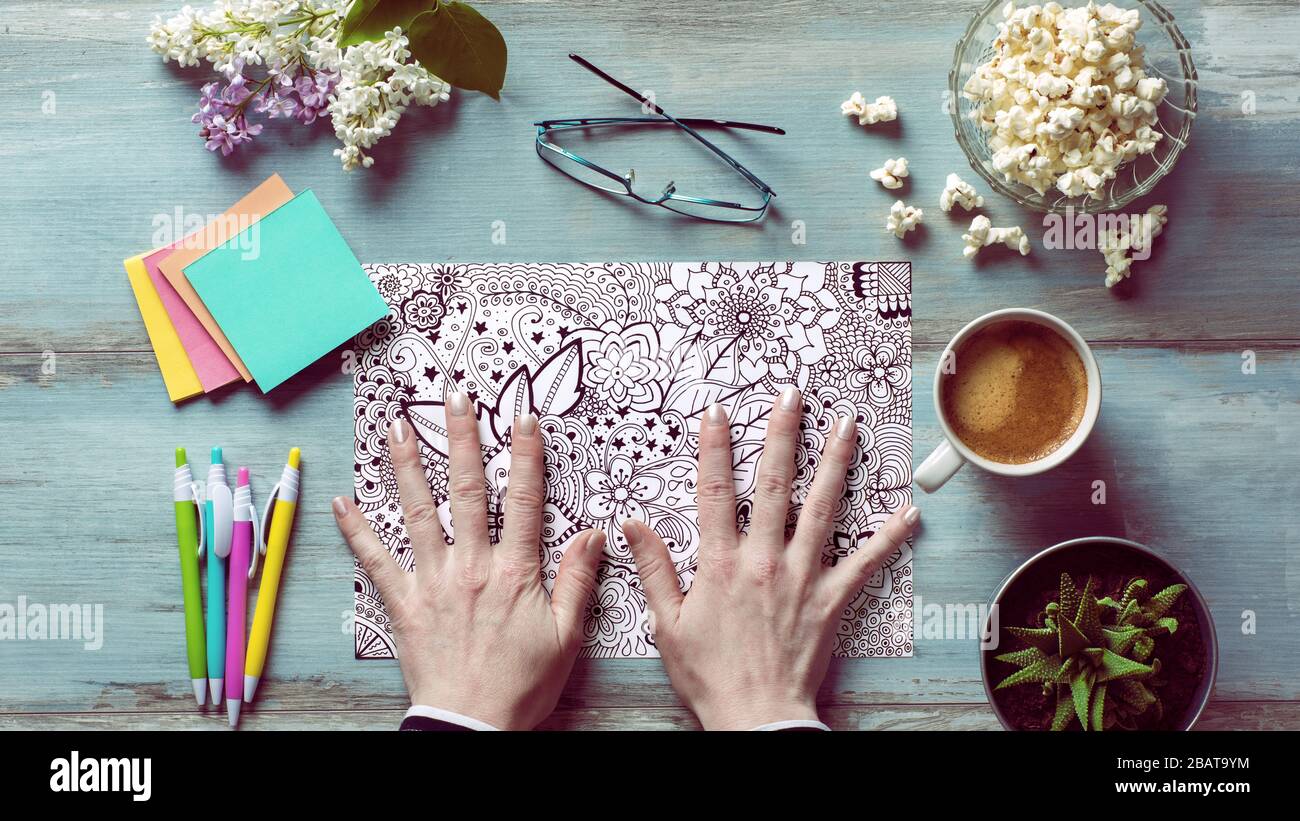 Adult coloring book, stress relieving trend. Art therapy, mental health, creativity and mindfulness concept. Flat lay close up on woman hands coloring Stock Photo