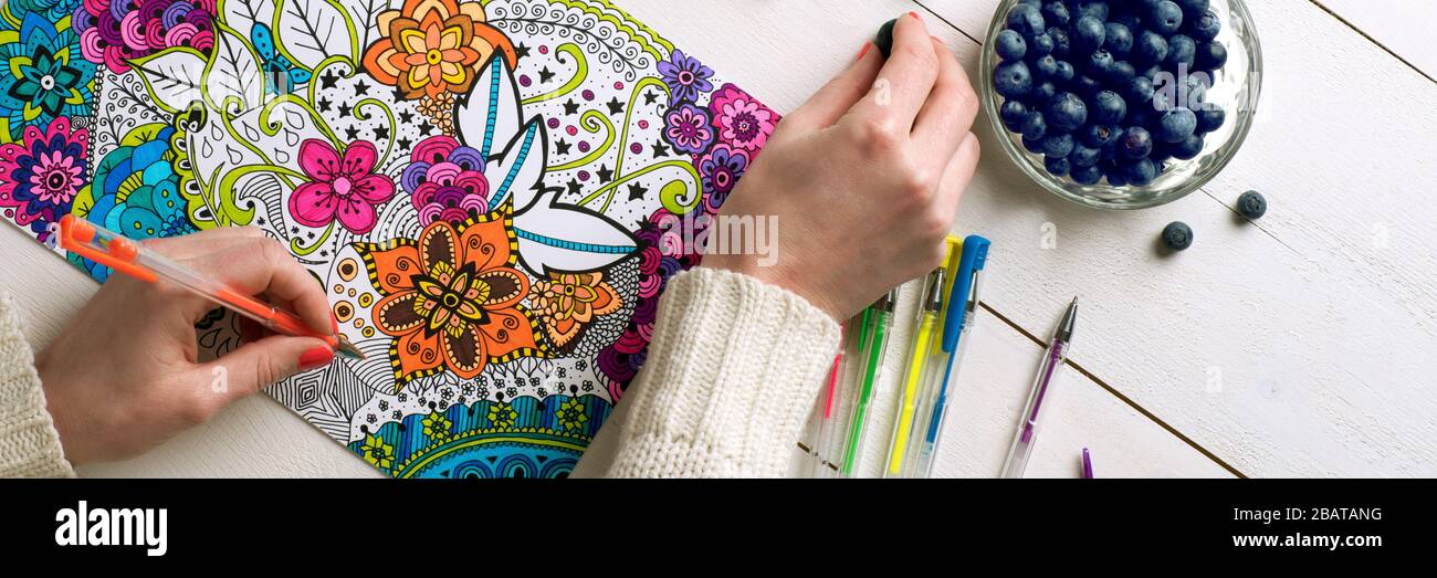 Adult coloring book, stress relieving trend. Art therapy, mental health, creativity and mindfulness concept. Flat lay close up on woman hands coloring Stock Photo