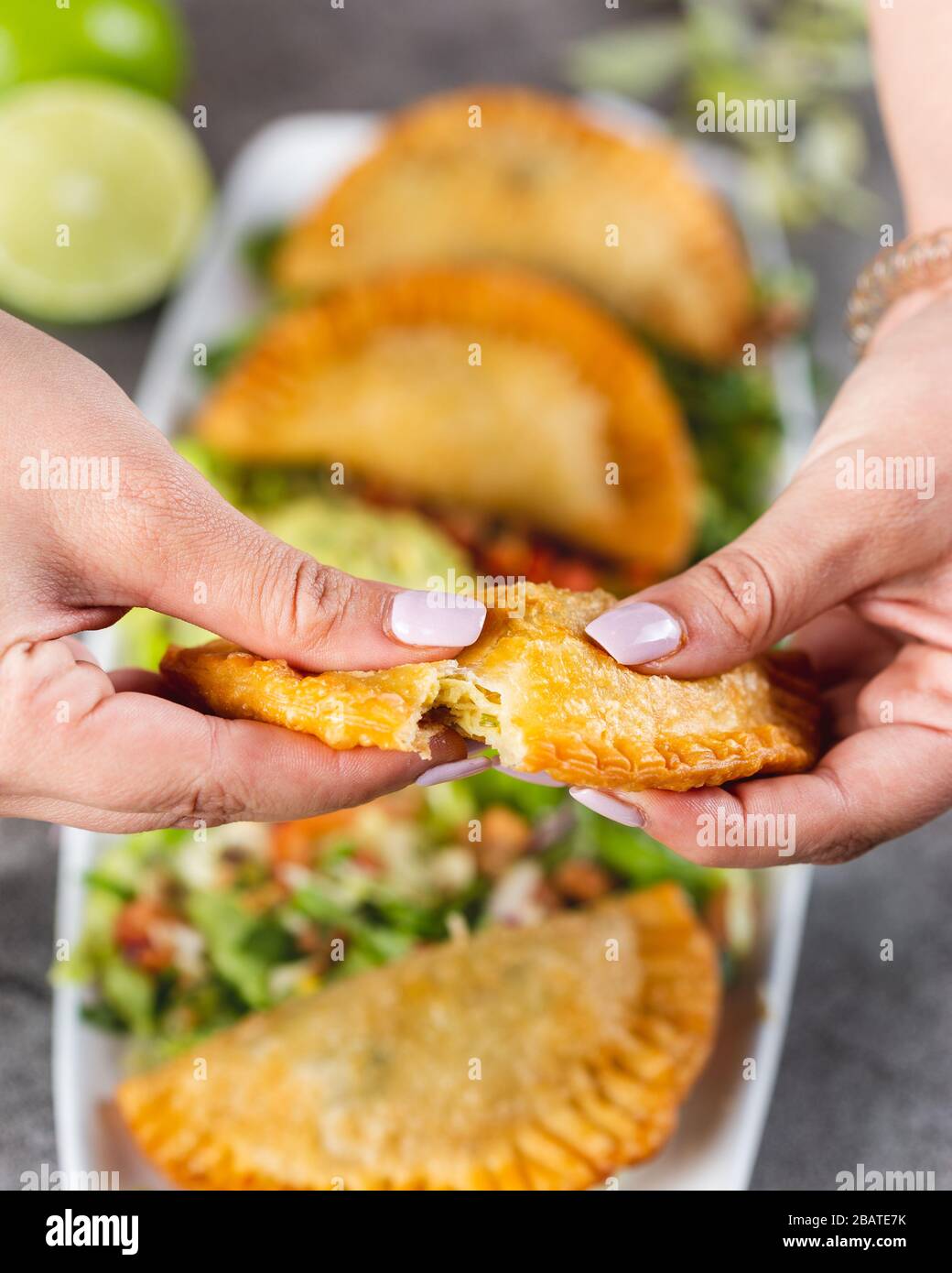 Young woman with pretty nails breaks open a fresh empanada over a plate of empanadas Stock Photo