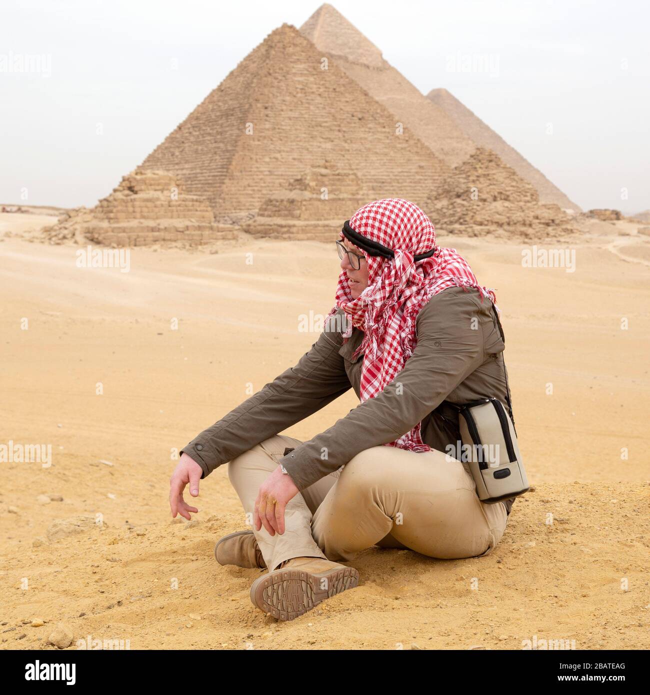 A tourist sitting in the desert wearing a traditional Middle-Eastern headdress while visiting the Giza Plateau at Cairo, Egypt. Stock Photo