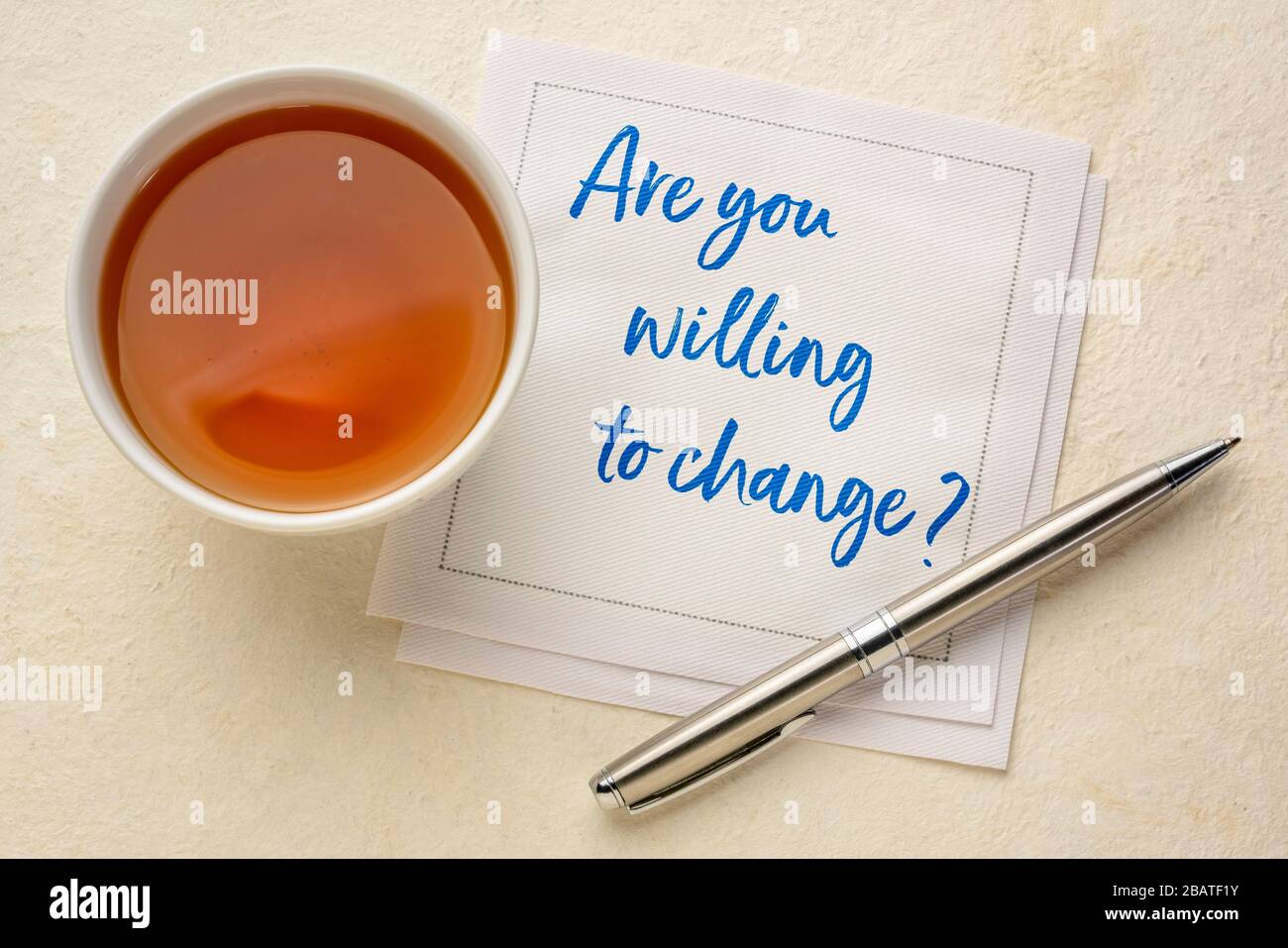 Are you willing to change? Handwriting on a napkin with a cup of tea. Self improvement and personal development concept. Stock Photo