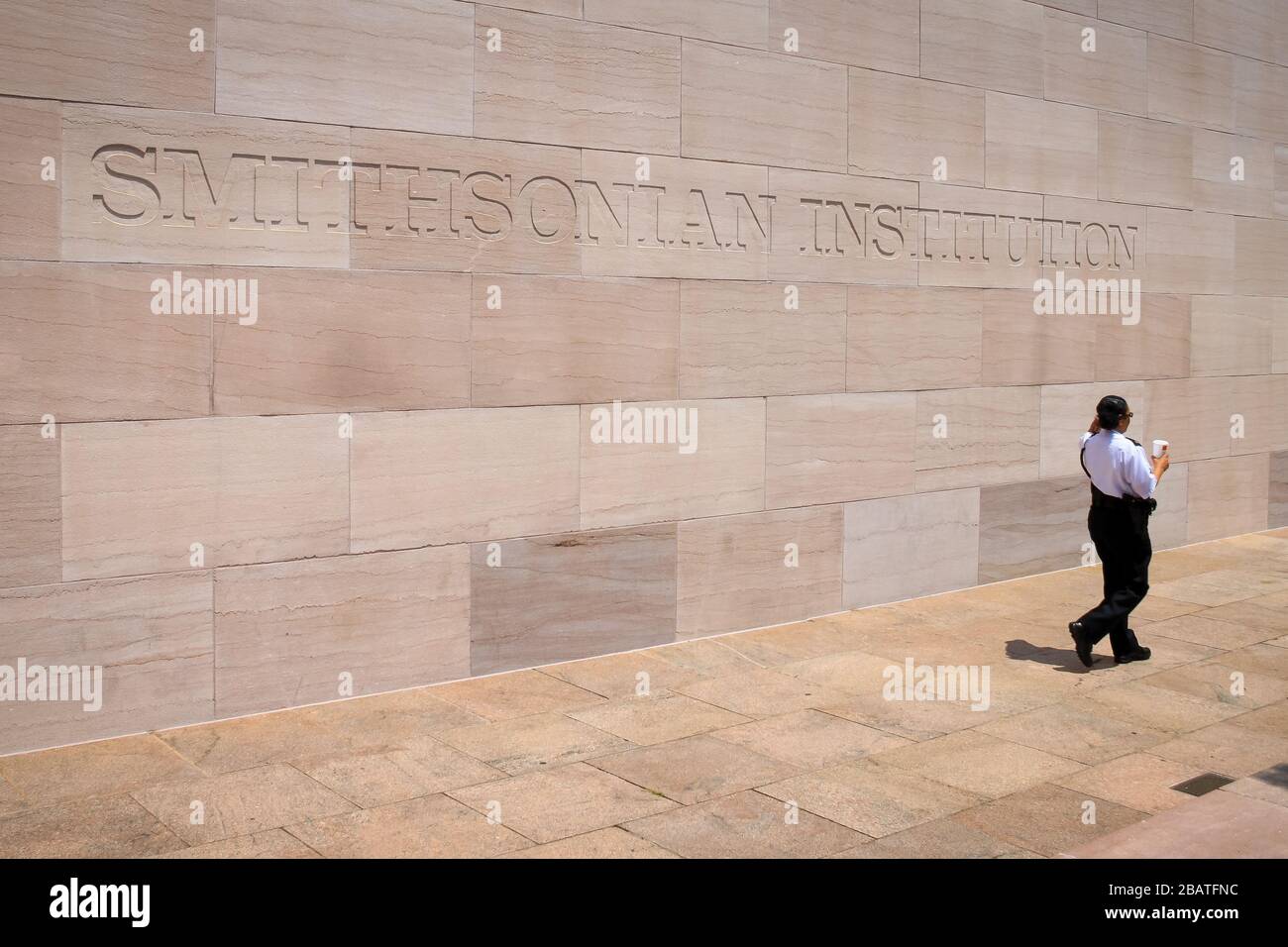 Smithsonian Institute sign on a wall at the National Mall in Washington DC, with a security guard passing in front of it. Stock Photo