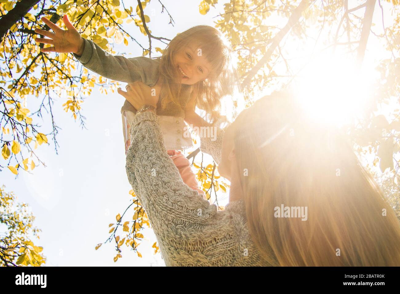 Closeup of beautiful young mother holding her little cheerful daughter in hands while having fun outdoors. Mom and her young child playing in autumn p Stock Photo