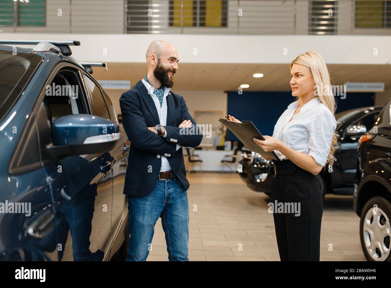 Smiling man and saleswoman in car dealership Stock Photo