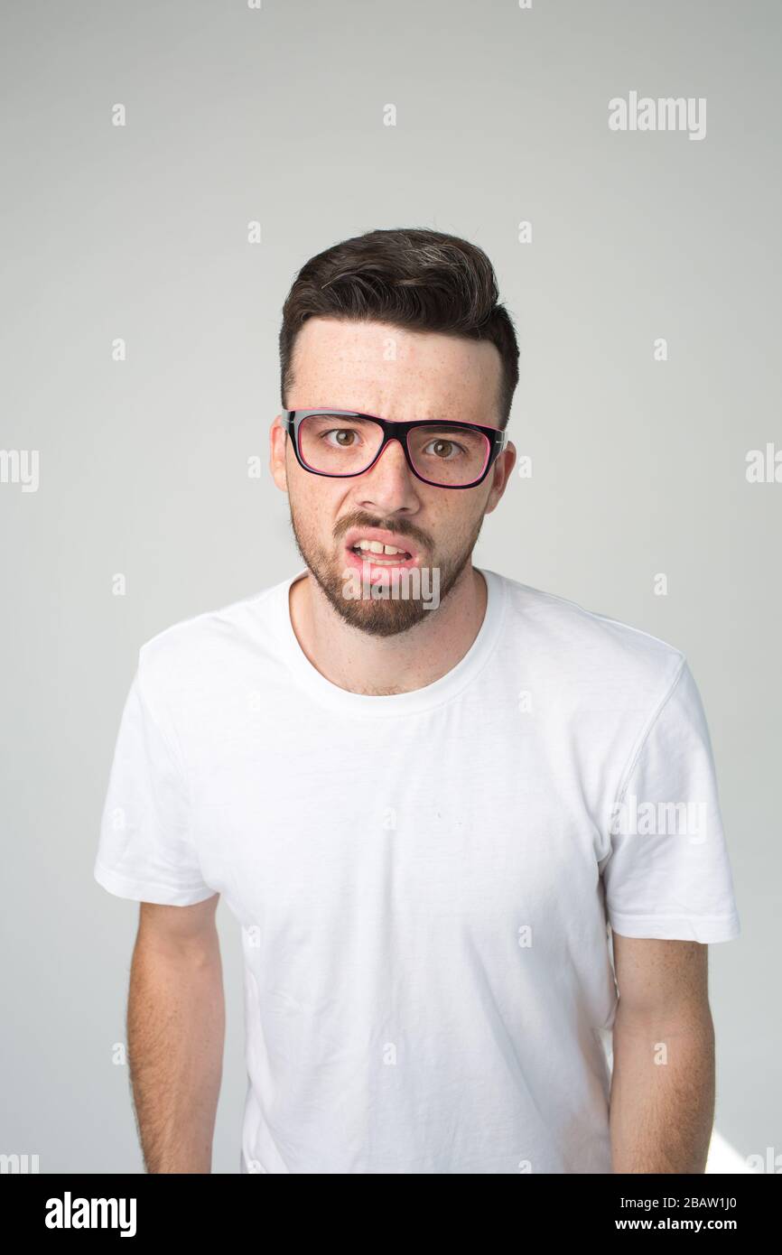 Young man isolated over background. Vertical picture of nerd or weirdo look straight through glasses. Boring and unhappy guy. Stand alon in white Stock Photo