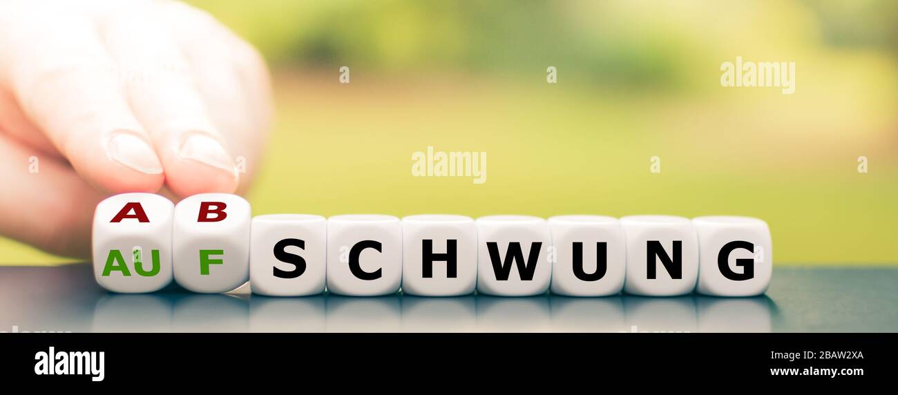 Symbol for a downswing of the economy. Hand turns dice and changes the German word 'Aufschwung' ('boom') to 'Abschwung' ('downswing'). Stock Photo