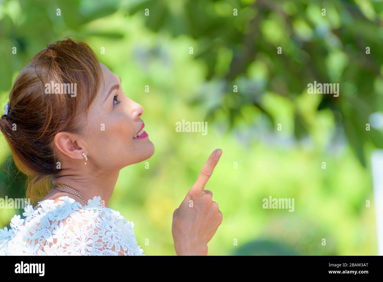 Side face of a beautiful woman healthy middle-aged Asian people dress in Thai style clothes, Portrait old lady relaxing outdoors pointing finger looki Stock Photo