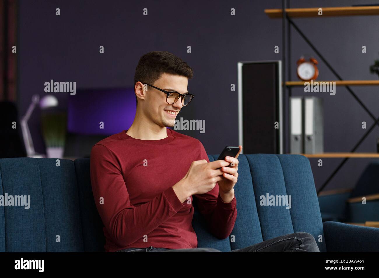 Young freelancer using smartphone and smiling. Happy man using m Stock Photo