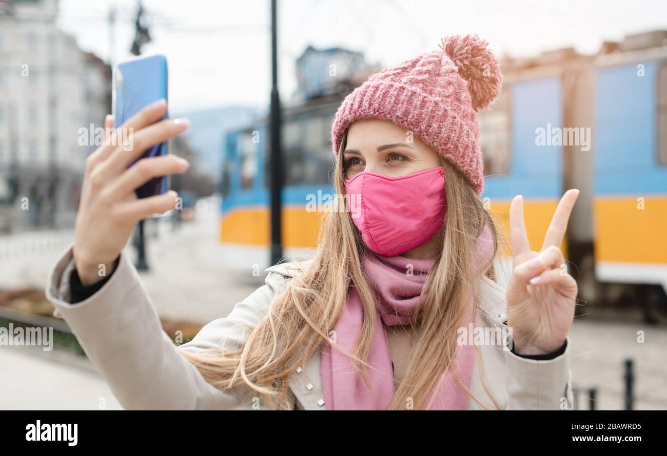 Woman doing victory sign making selfie with phone wearing mask Stock Photo