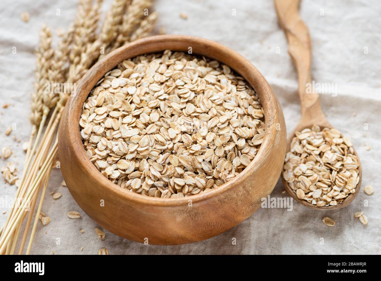 Rolled oats in wooden bowl on linen background. Healthy food, clean eating concept. Breakfast food uncooked oatmeal Stock Photo