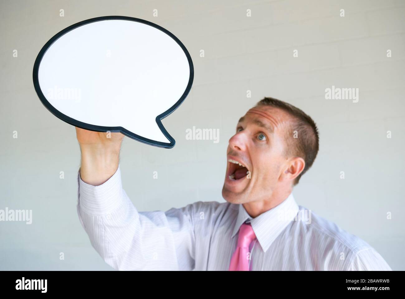 Enthusiastic businessman holding up a blank speech bubble shouting a message into copy space Stock Photo