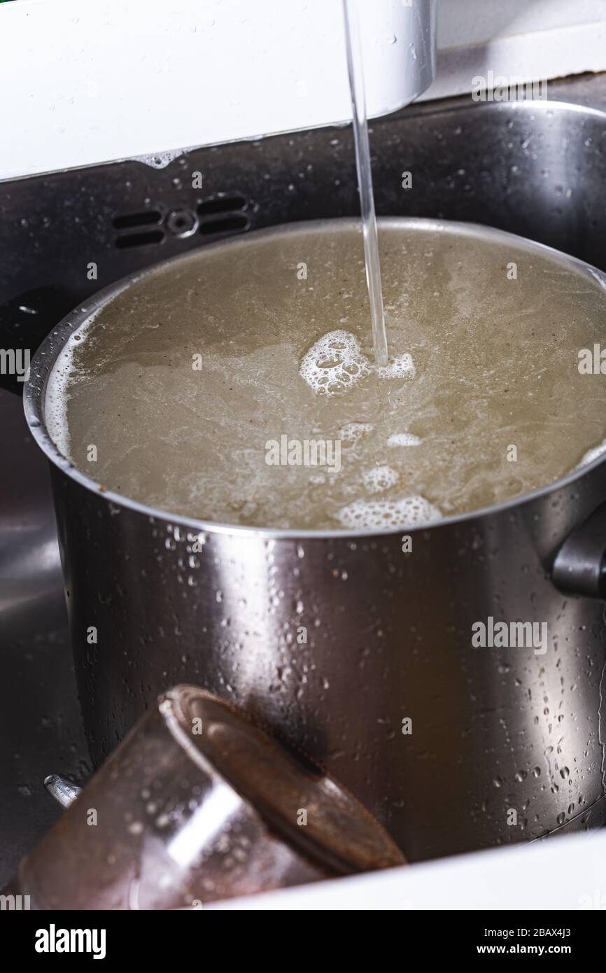 https://c8.alamy.com/comp/2BAX4J3/pouring-water-into-a-big-dirty-stainless-pot-after-cooking-on-a-kitchen-sink-2BAX4J3.jpg