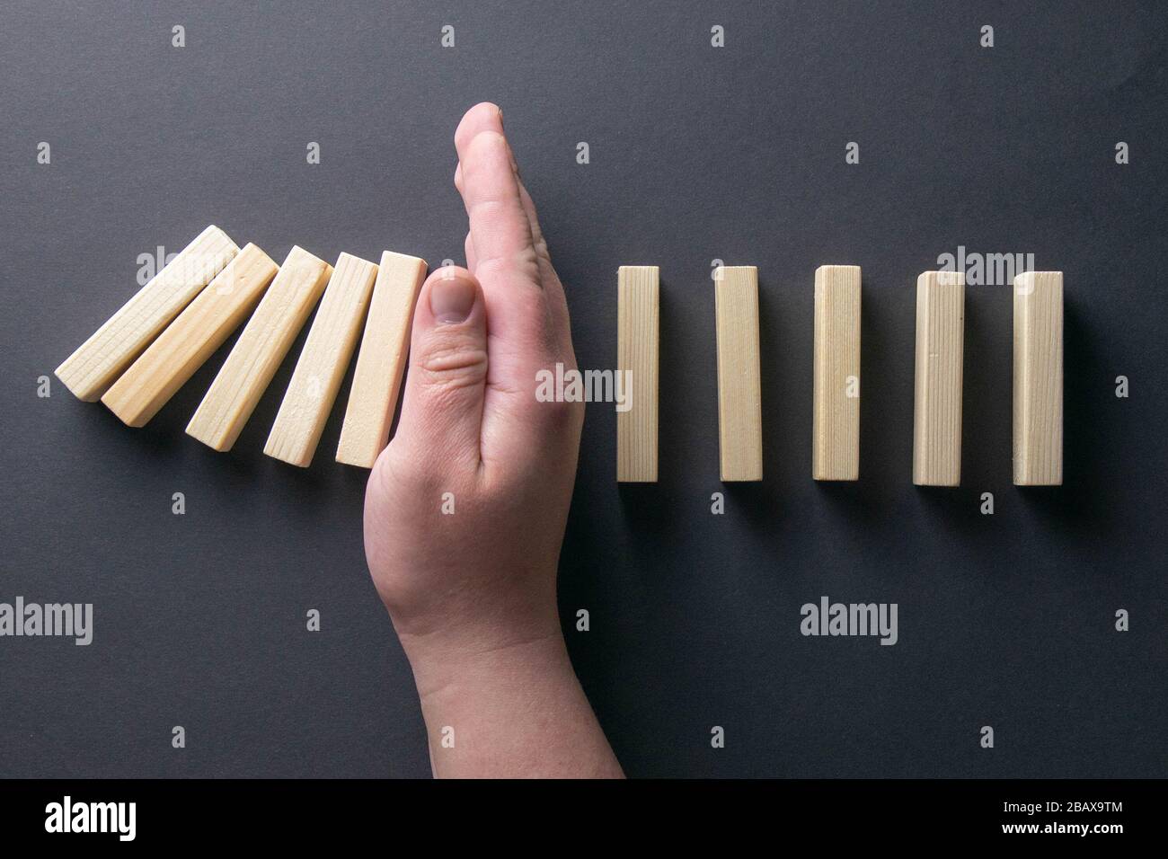 Top view man hand stopping falling dominos in a business crisis management conceptual image Stock Photo