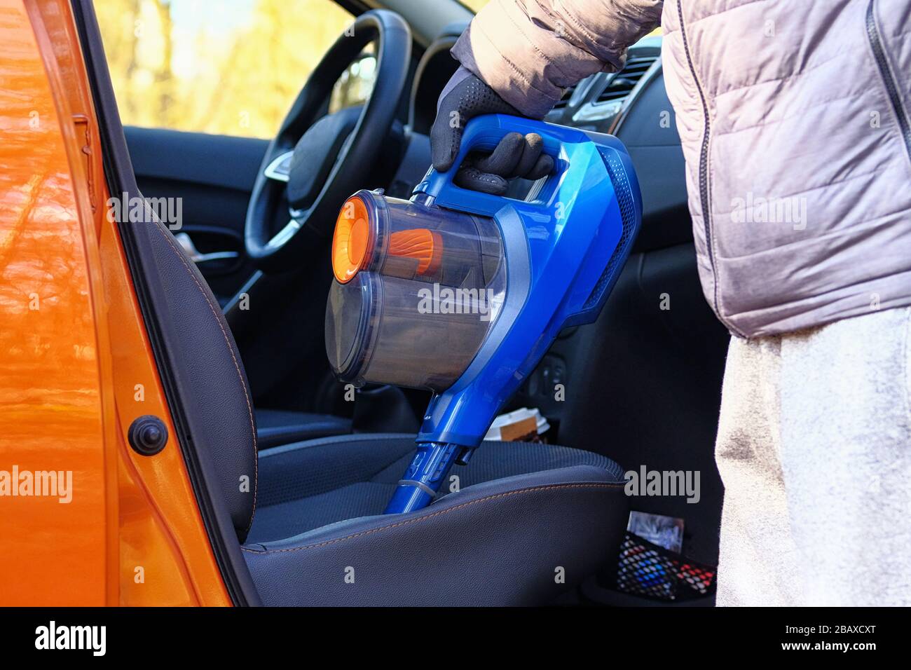 Vacuum cleaner in hands of driver. Cleaning of interior of automobile