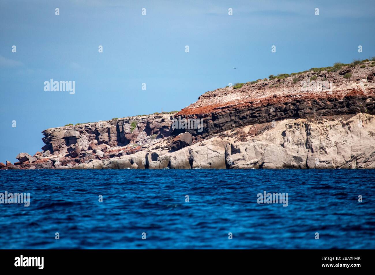 The rocks forming a small mountain with different layers of sediments formed different colors with the blue Cortez sea on the bottom Stock Photo
