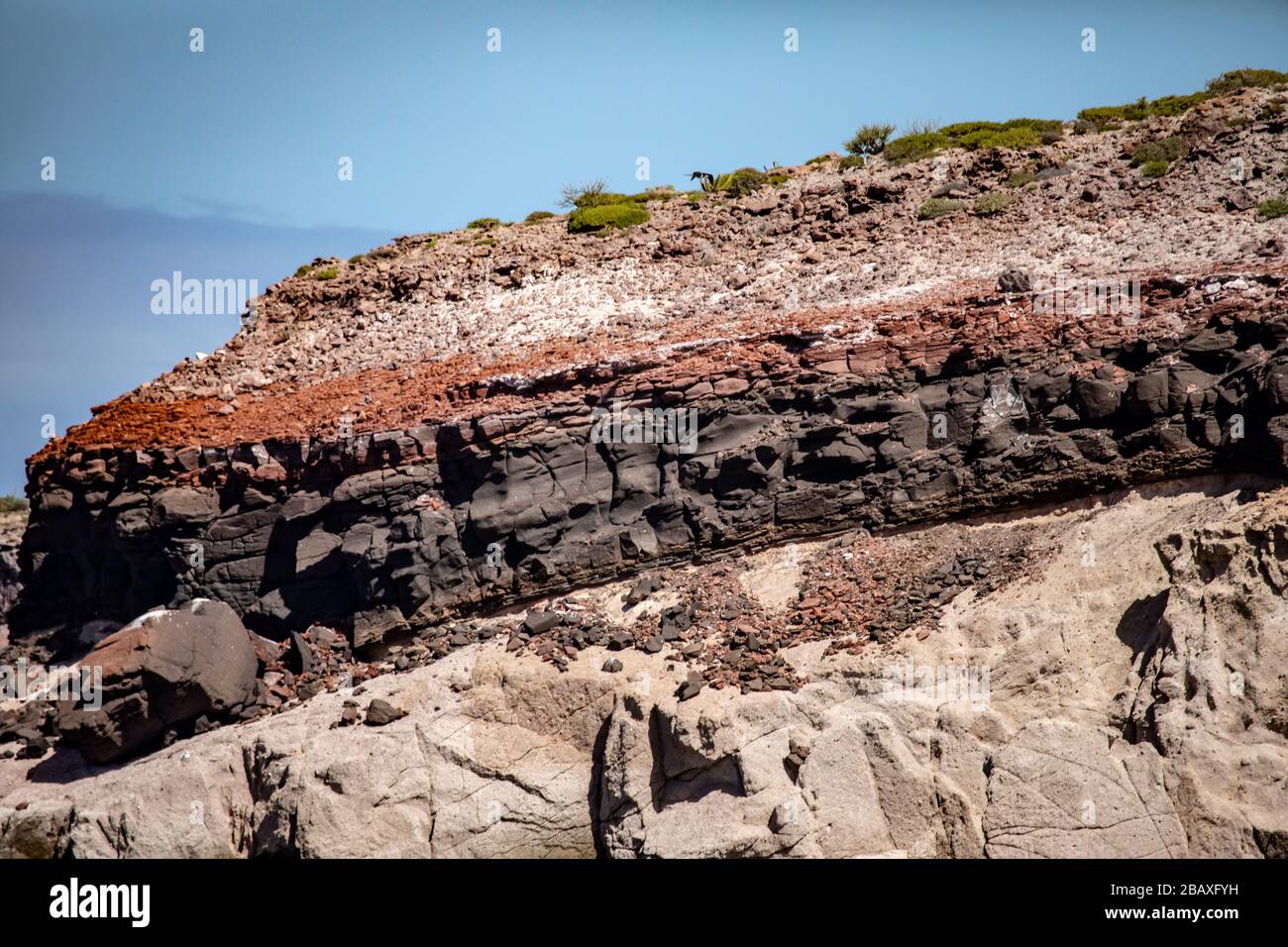 The rocks forming a small mountain with different layers of sediments formed different colors with the blue Cortez sea on the bottom Stock Photo