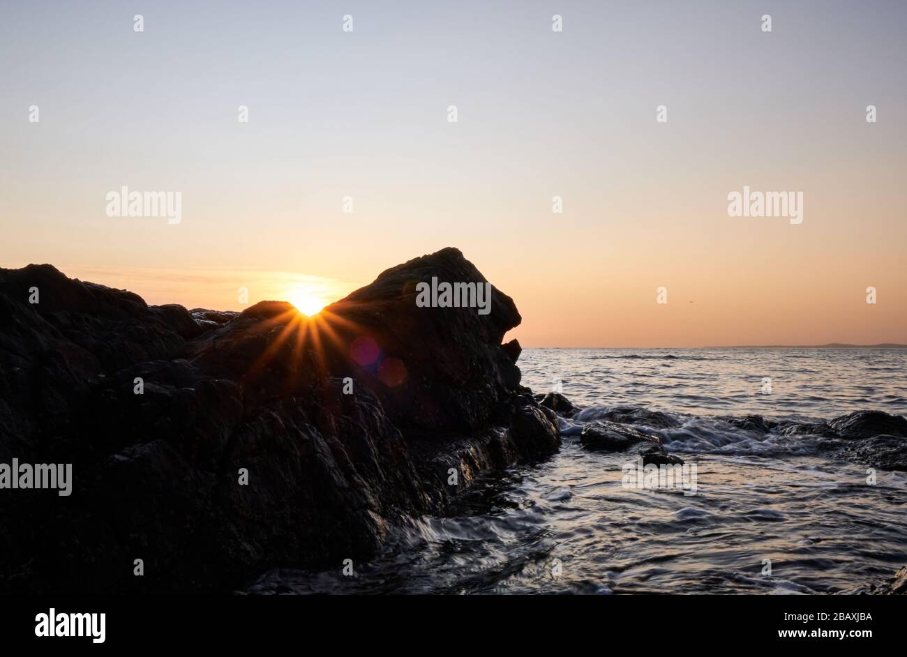 View of the sun burst or the star sun over the rock with the sunset at the background in the atlantic ocean, Punta Ballena, Maldonado, Uruguay Stock Photo