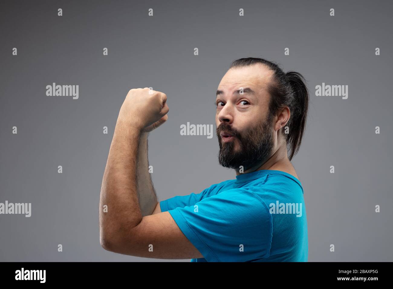 Happy looking bearded man in blue t-shirt and with combed long black hair, expressing winning gesture with his hands up and fists clenched. Close-up s Stock Photo