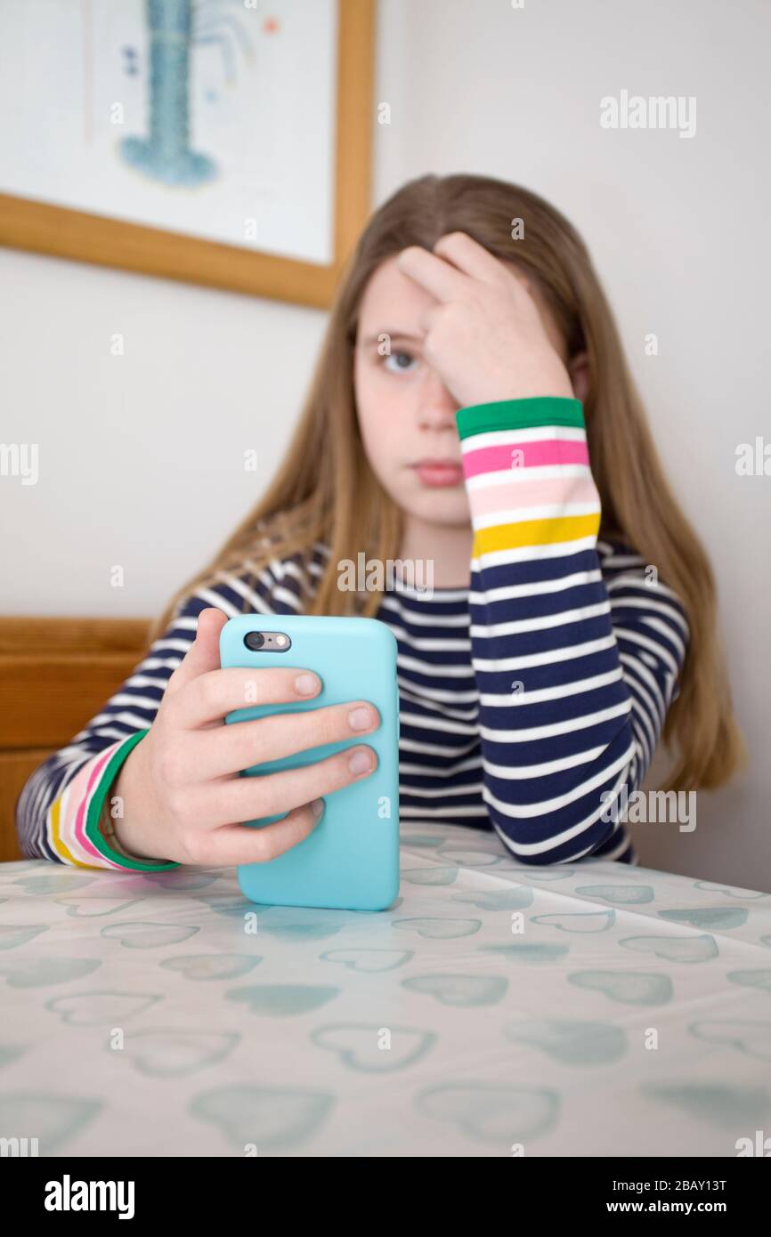 Young girl with head in hand holding her iPhone sat at the table, England Stock Photo
