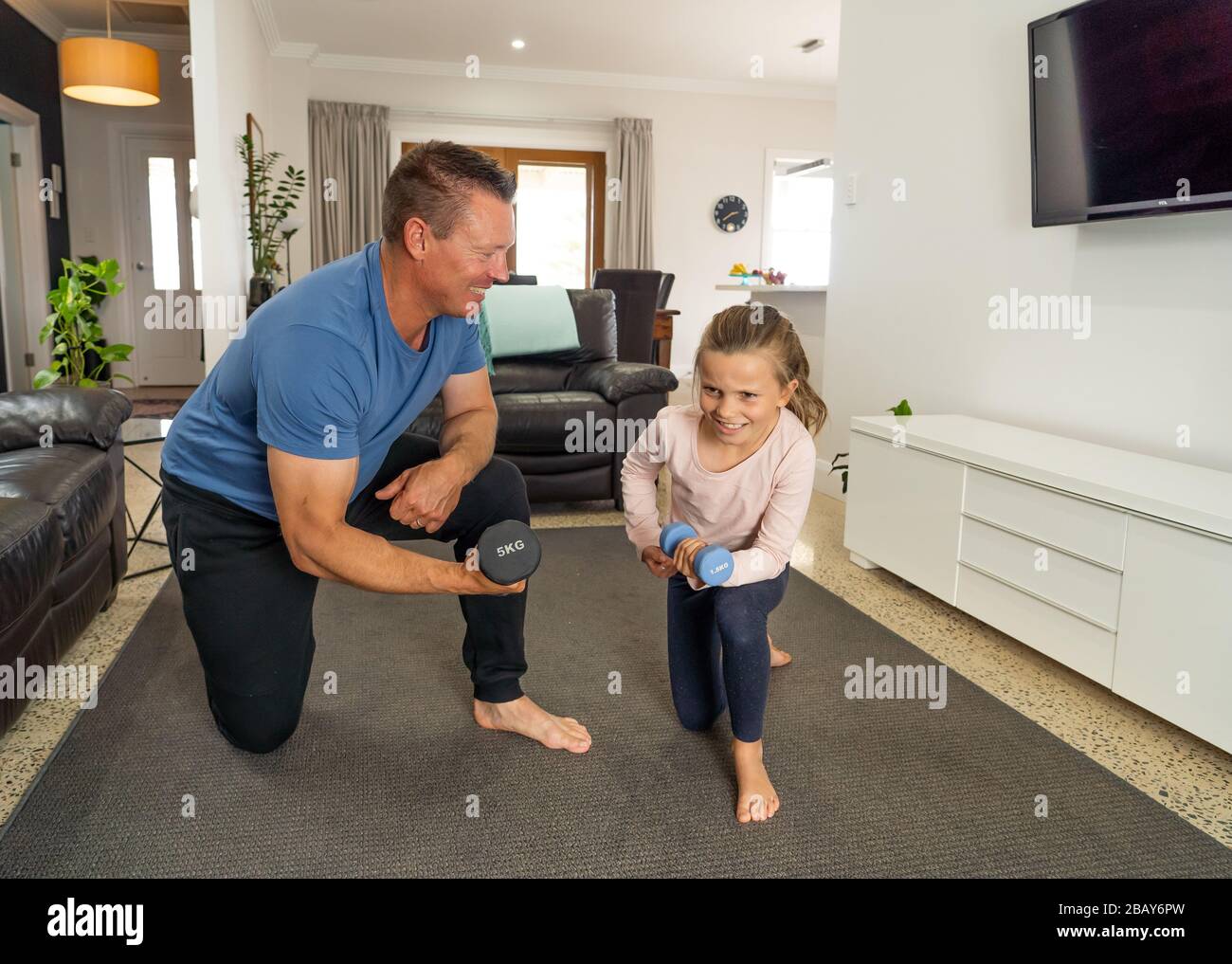 COVID-19 shutdown. Father and daughter in quarantine exercising together with dumbbells. Benefits of physical activity during lockdown. Stay at home, Stock Photo