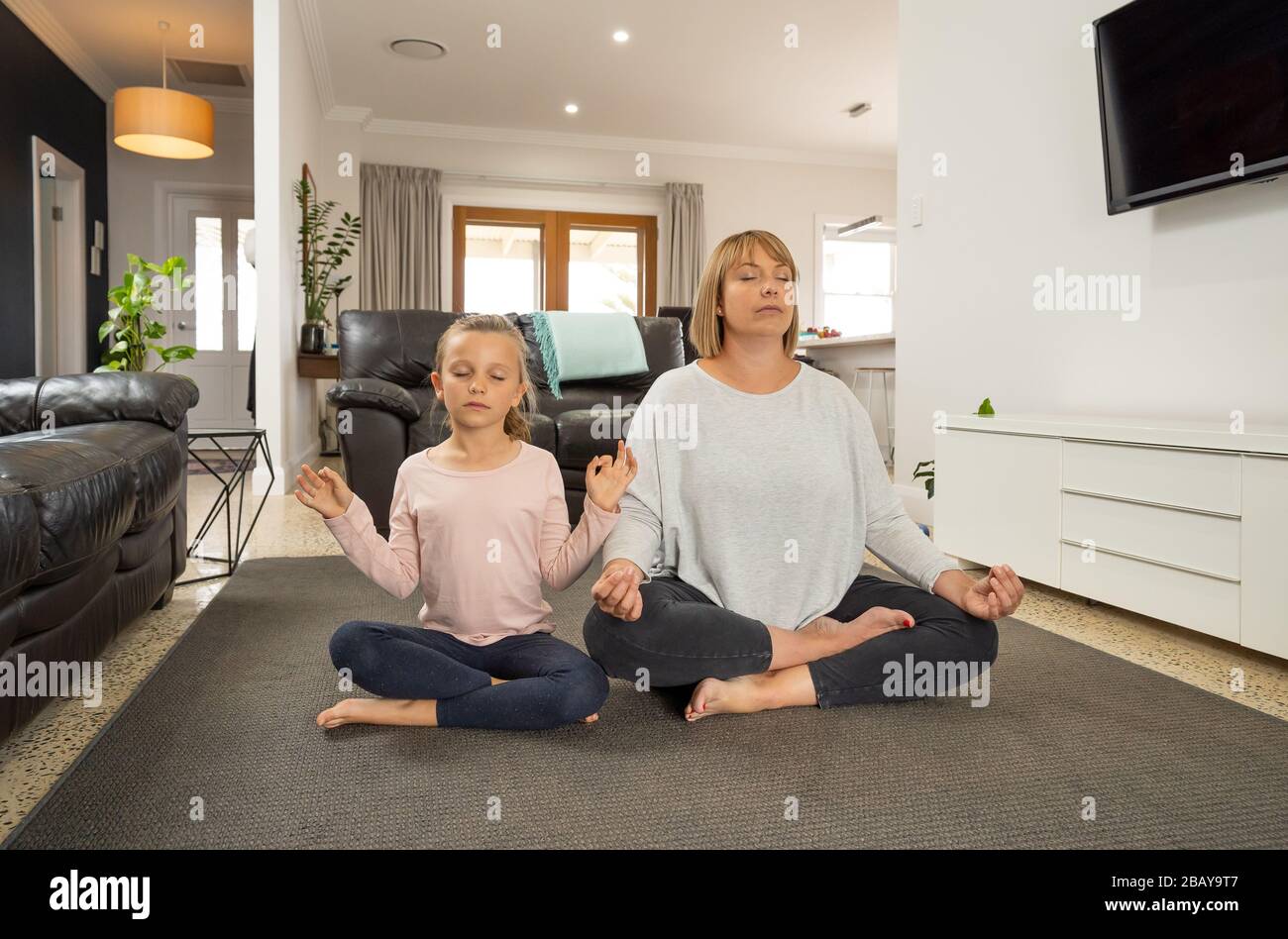 COVID-19 Shutdown. Mother and daughter in quarantine doing yoga indoors. Mother and daughter doing meditation during lockdown. Health, exercise stay a Stock Photo