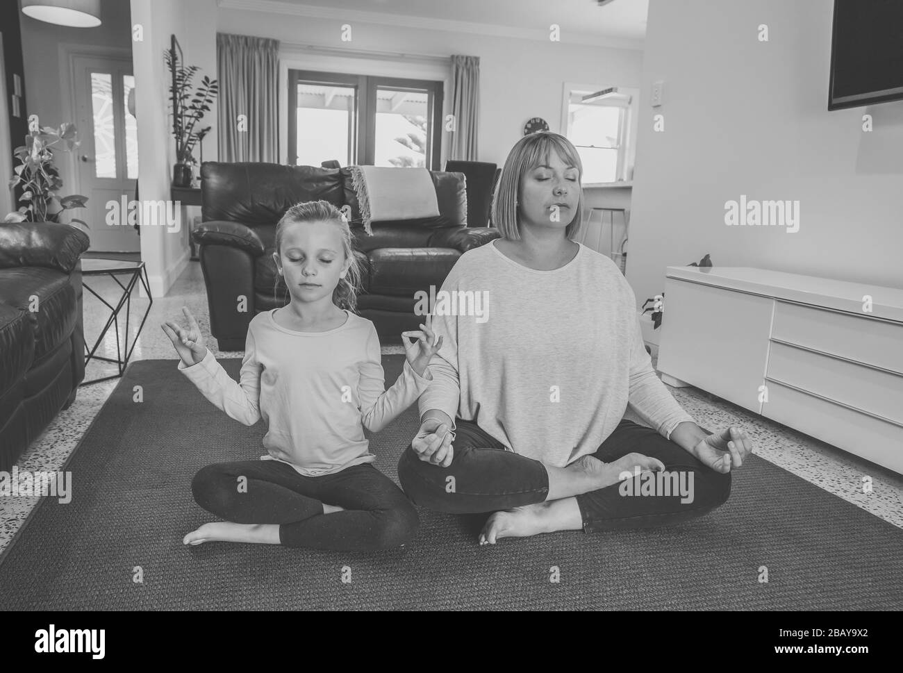 COVID-19 Shutdown. Mother and daughter in quarantine doing yoga indoors. Mother and daughter doing meditation during lockdown. Health, exercise stay a Stock Photo