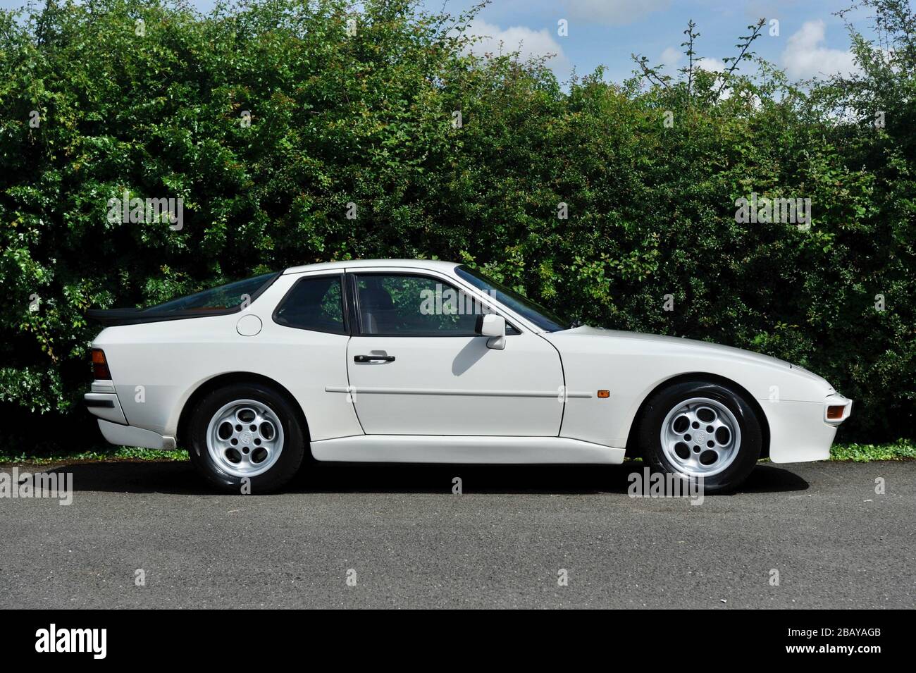 White Porsche 944 side profile shot against a green hedgerow