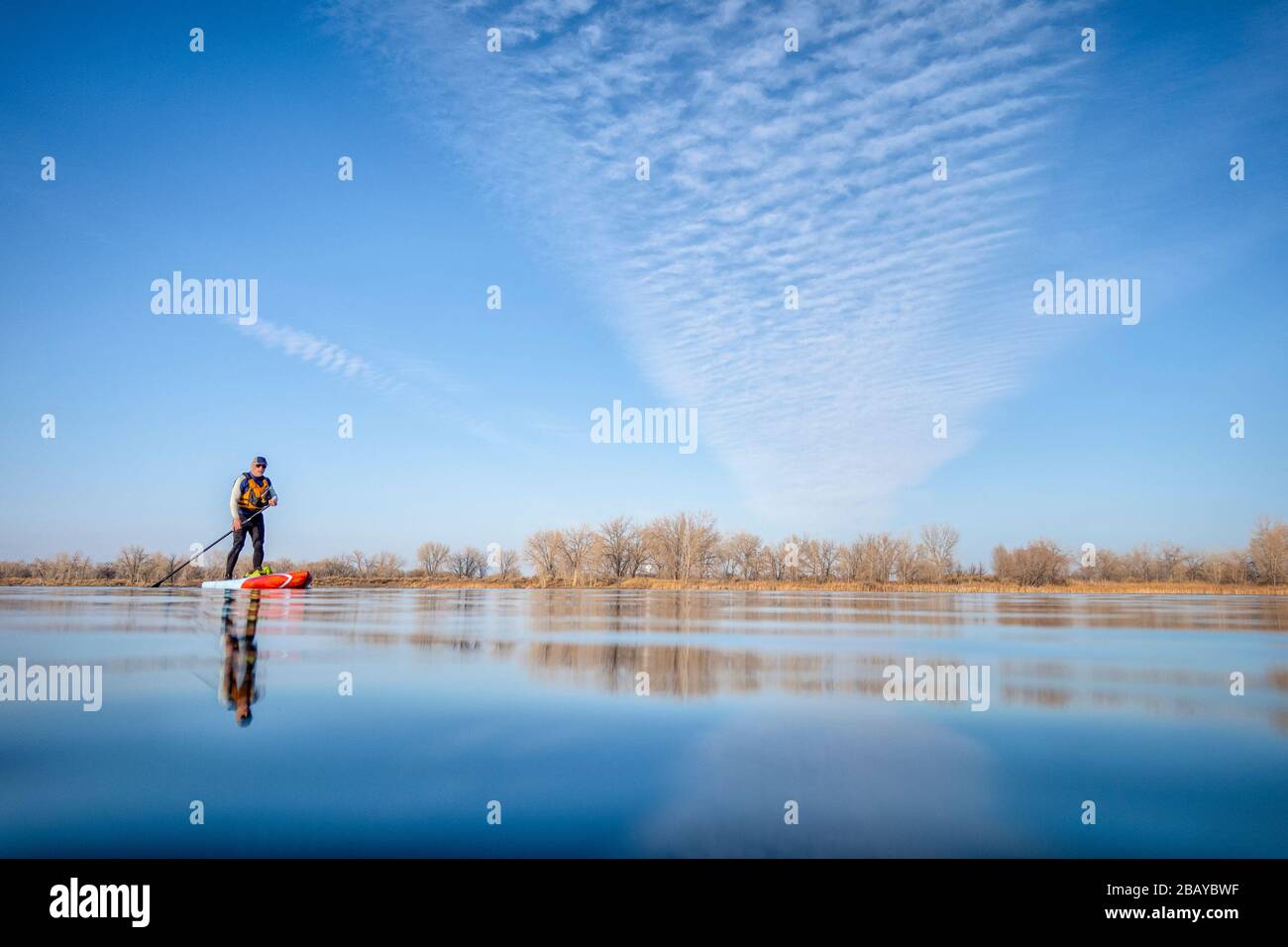 senior male paddler in a wetsuit is paddling a stand up paddleboard on