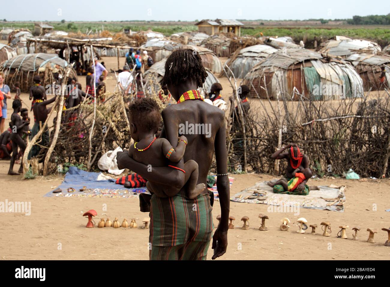 Rear View of a Dassanech Woman with a Baby on her Hip and her Village as a Backdrop Stock Photo