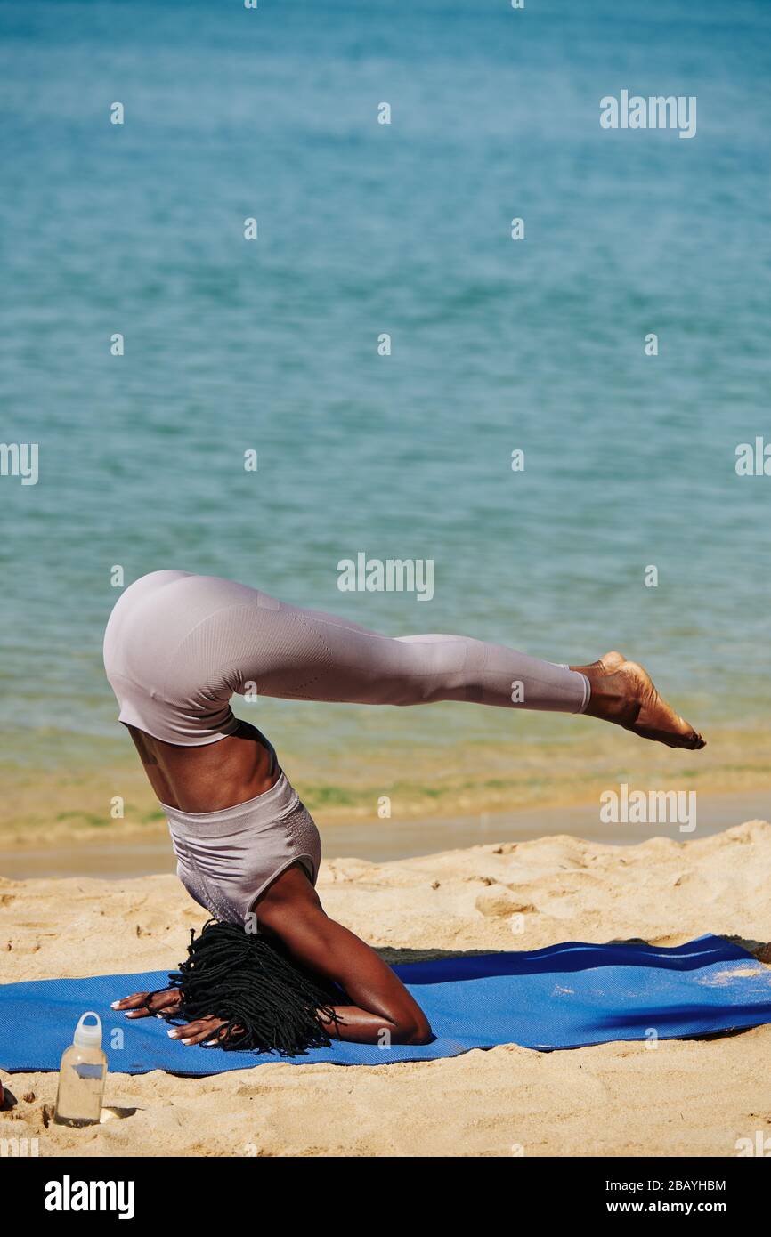 Strong fit young woman doing supported headstand on the beach Stock Photo