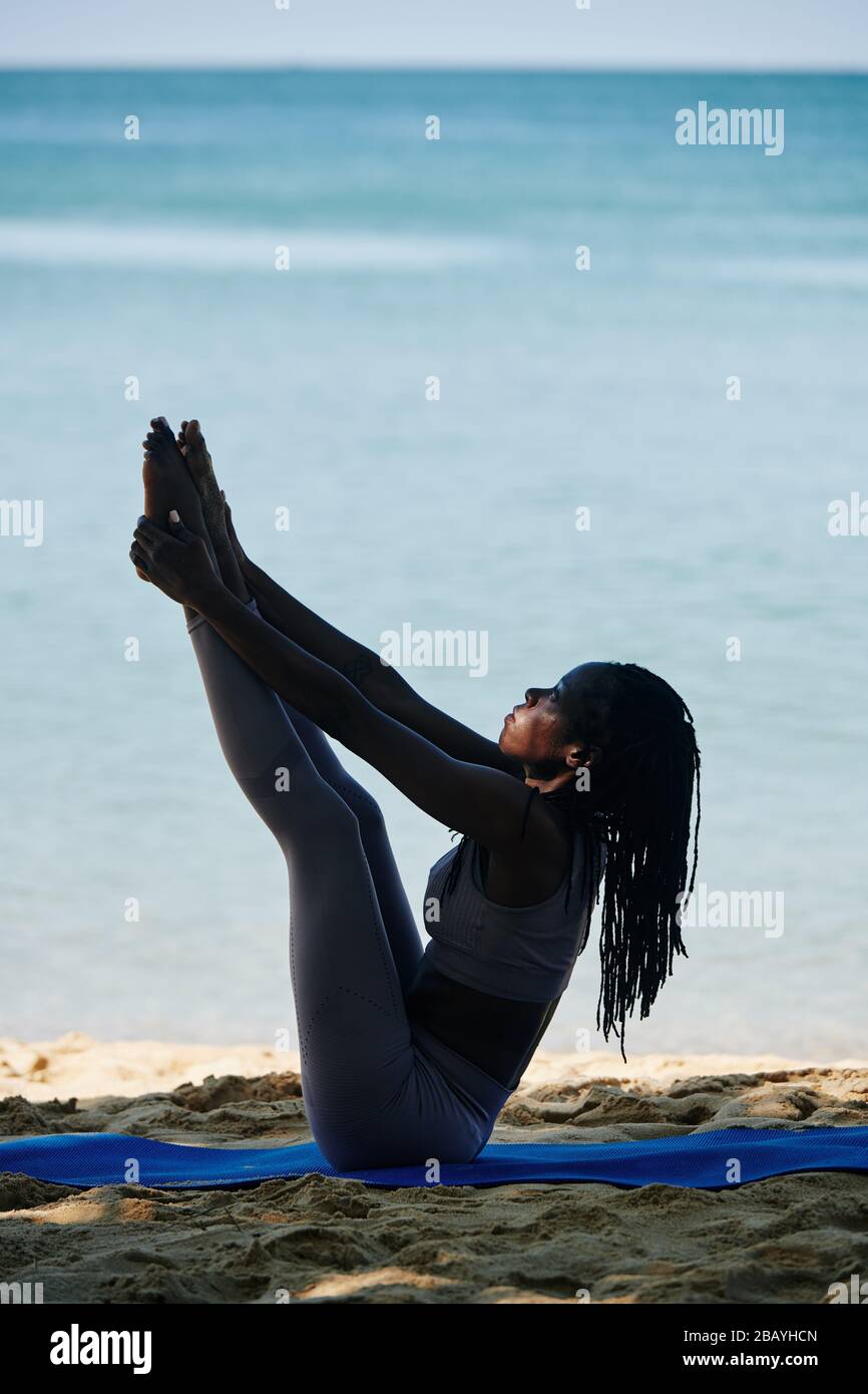Young fit Black woman in seated balancing yoga pose exercising on