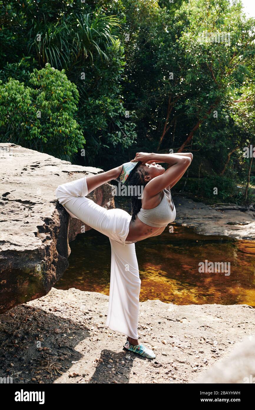 Flexible woman doing advanced yoga backbends when standing on rock in forest Stock Photo