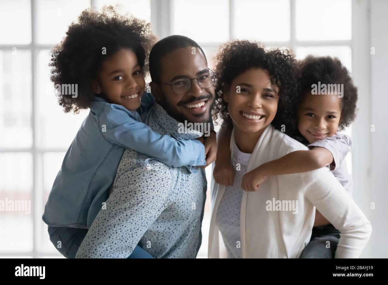 Portrait of African ethnicity parents piggybacking son and daughter indoors Stock Photo