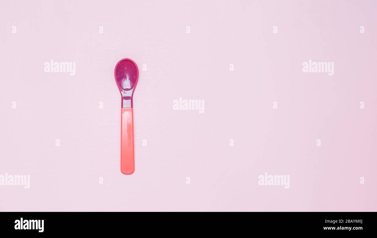 pink and purple plactic color Baby spoon on pink background flatlay Stock Photo