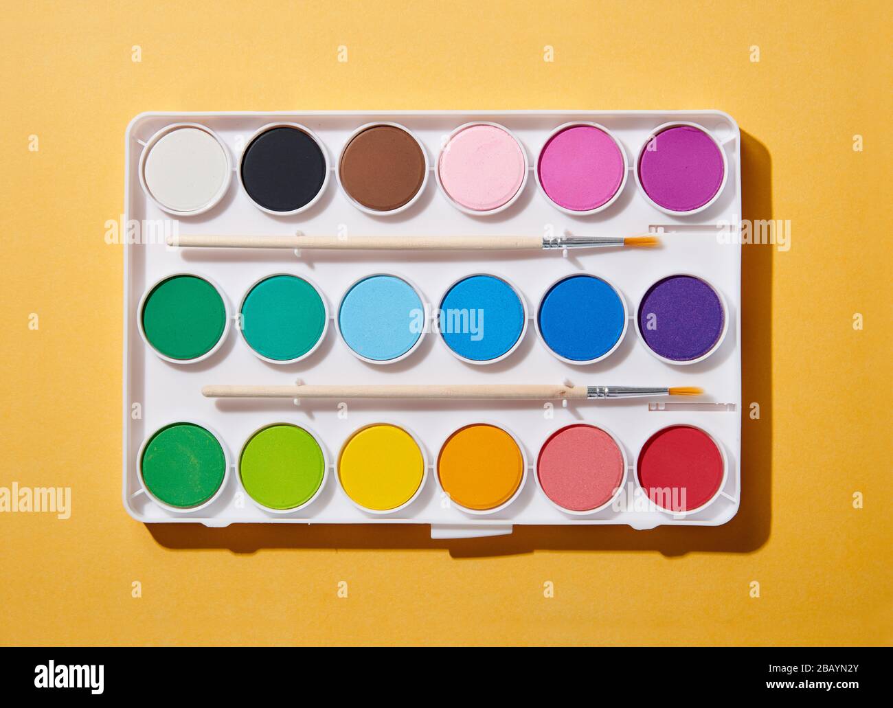 Open new watercolor paint box with two brushes and rainbow colored paints viewed from above on an orange background Stock Photo