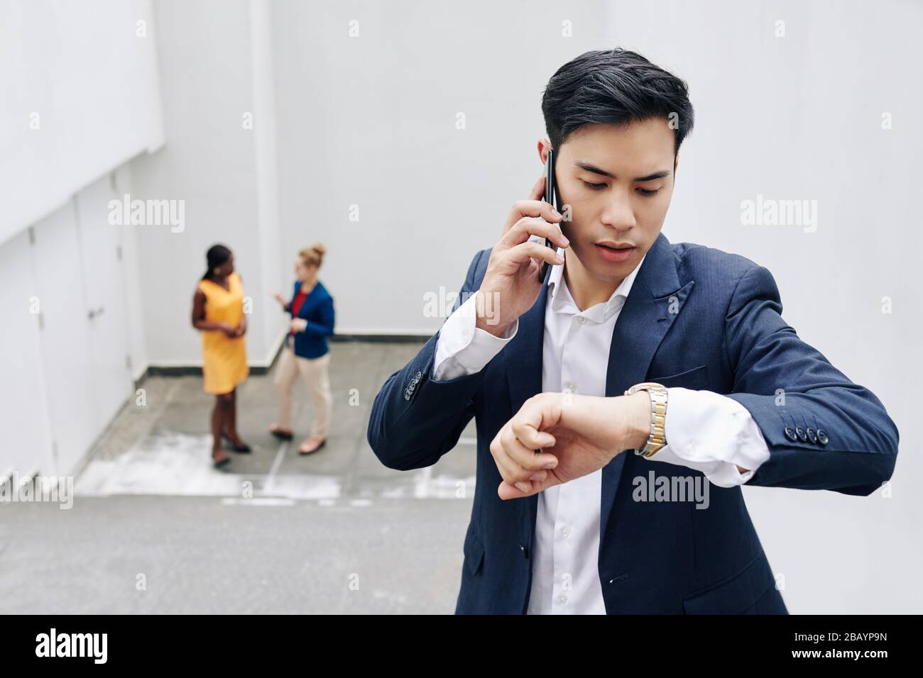 Young Asian businessman talking on phone and checking time on his wrist watch Stock Photo